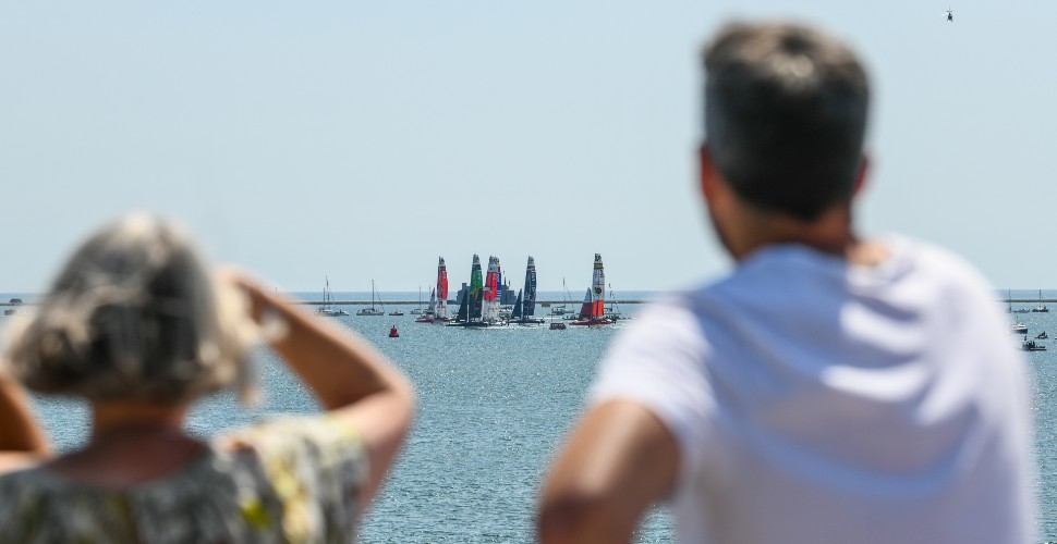 Two people facing out to sea, watching the SailGP racing in Plymouth in the waters of Plymouth Sound with the Breakwater in the distance